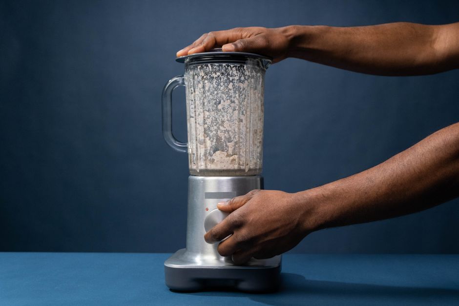 Close-up of male hands operating a blender in a kitchen setting.